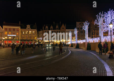 Menschen auf dem großen Marktplatz (Markt) im Zentrum von Brügge, Nacht. Mittelalterliche Häuser sind mit Weihnachtsbeleuchtung, wintermärchen eingerichtet Stockfoto