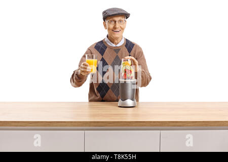 Fröhlicher älterer Mann Vorbereitung Obst in einen Mixer und halten ein Glas frischen Saft auf weißem Hintergrund Stockfoto