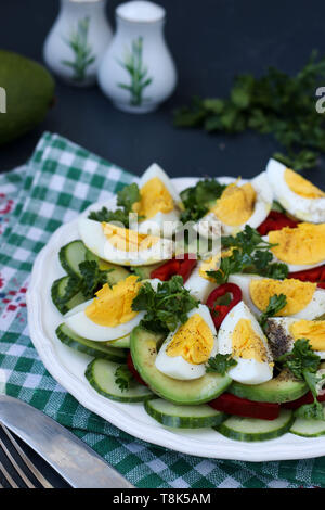 Nützliche Salat mit Avocado, Gurken, Eier und Paprika in einer Platte gegen einen dunklen Hintergrund entfernt, vertikale Foto Stockfoto