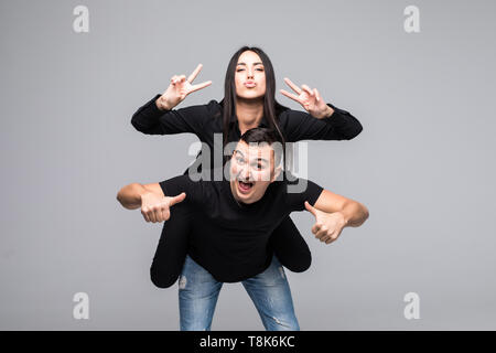 Junge lustig Paar, Freund piggy backing Freundin, Mädchen, Frieden Zeichen mit den Händen über grauer Hintergrund Stockfoto