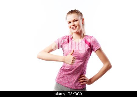 Eine dunkelhaarige Frau Trainer in einem sportlichen Rosa kurze T-Shirts und Shorts zeigt Daumen hoch und Lächeln auf weißem Hintergrund isoliert im Studio Stockfoto