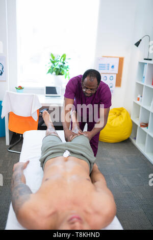 Massage therapist in Uniform massieren Beine für Sportler Stockfoto
