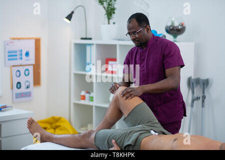 Massage Master in Gläsern und einheitliche massieren Bein für Mann in Shorts Stockfoto