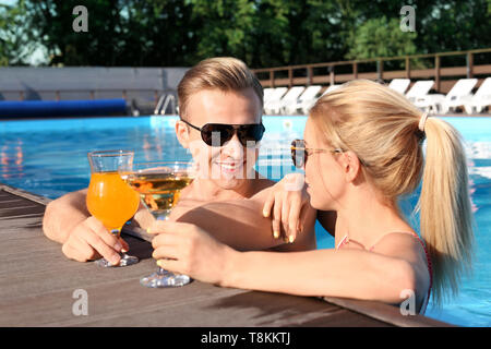 Glückliches junges Paar trinken Cocktails in Pool im Resort Stockfoto