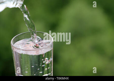 Sauberes Wasser gießt aus einer Flasche in Glas auf grüne Natur Hintergrund. Konzept der Gesundheit und Frische, Durst, Wasserreinigung, Ökologie Stockfoto