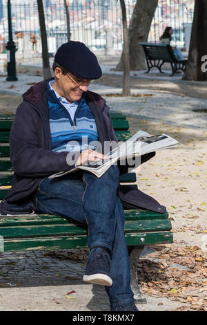 Jardim de São Pedro de Alcântara, Lissabon, Portugal: ein Mann sitzt auf einer Parkbank, durch einen Artikel in der Zeitung amüsiert Stockfoto
