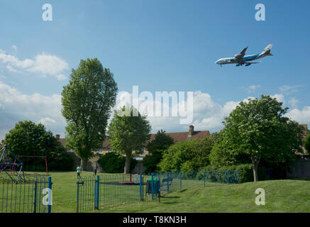 Tief fliegender Passagier- und Flugzeug über Wohnhäuser und Kinderspielplatz in der Gemeinde von Hounslow, Heathrow Flughafen zu landen Stockfoto