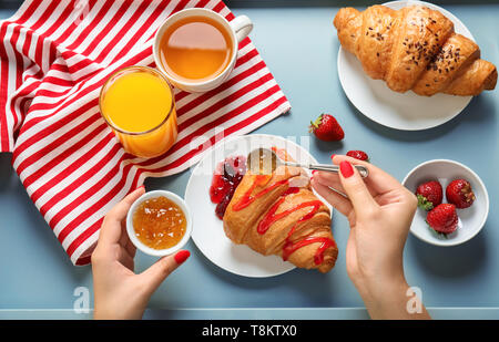 Junge Frau gießen leckere Croissant mit Marmelade auf Platte Stockfoto
