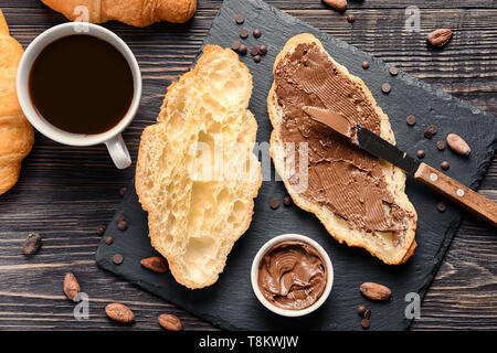 Leckere Croissants mit Schokolade einfügen und Tasse Kaffee auf hölzernen Tisch Stockfoto