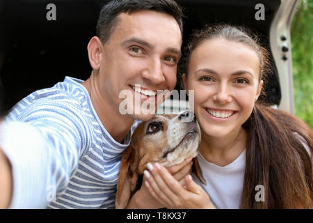 Junges Paar mit niedlichen Hund in der Nähe von selfie Auto im Freien Stockfoto