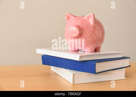 Piggy Bank und Stapel von Büchern auf hellem Holztisch Stockfoto