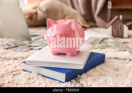 Sparschwein mit Büchern auf einem weichen Teppich im Innenbereich Stockfoto