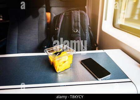 Wassermelonen Salat mit der Gabel - Reisen in schnellen Bahn in Großbritannien kleine Smartphone auf dem Tisch Stockfoto