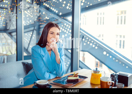 Begeisterte Frau in trendigen Herbst Outfit im gemütlichen Cafe chillen, Tagträumen. Glückliche Gefühle. Reisen Person. Hispanische Mädchen tragen formalen Blau sui Stockfoto