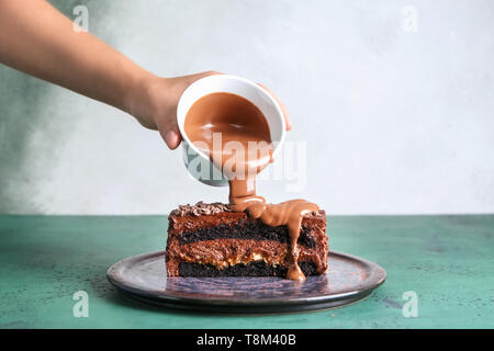 Frau gießen Schokolade Soße auf Stück leckeren Kuchen auf Farbtabelle Stockfoto