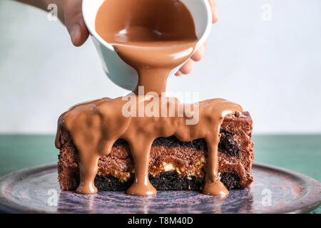 Frau gießen Schokolade Soße auf Stück leckeren Kuchen auf Farbtabelle Stockfoto