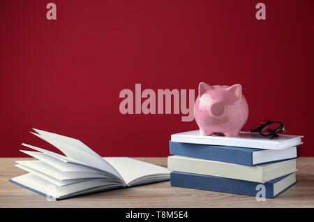 Cute Sparschwein auf Stapel von Büchern gegen Farbe Hintergrund Stockfoto