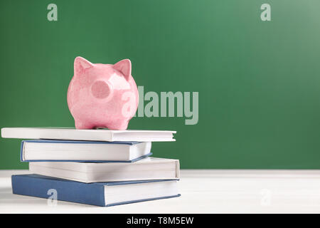 Cute Sparschwein auf Stapel von Büchern gegen Farbe Hintergrund Stockfoto