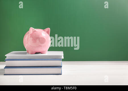 Cute Sparschwein auf Stapel von Büchern gegen Farbe Hintergrund Stockfoto