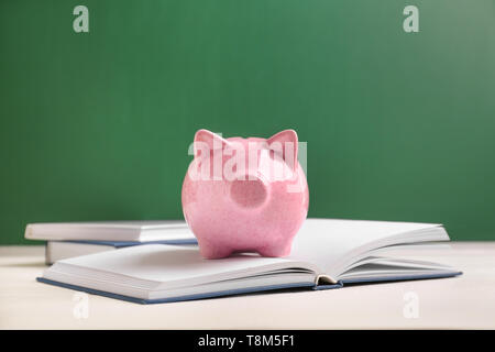 Cute Sparschwein mit Büchern auf dem Tisch gegen Farbe Hintergrund Stockfoto