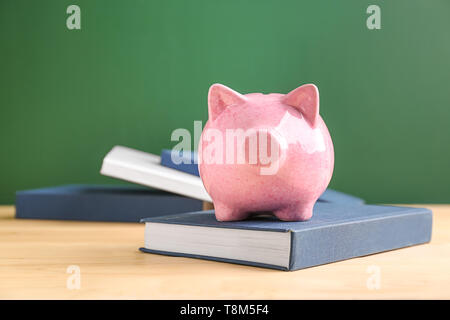 Cute Sparschwein mit Büchern auf dem Tisch gegen Farbe Hintergrund Stockfoto