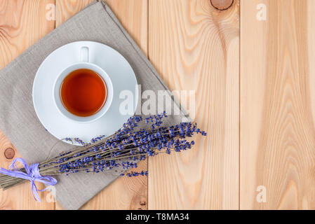 Eine Tasse wohltuenden Tee mit Lavendel und ein Bündel von Blumen auf einer Leinwand Serviette auf Holzbohlen, Ansicht von oben; auf der rechten Seite ist Platz für eine Inschrift Stockfoto
