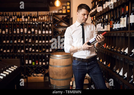 Attraktive sommelier tragen weiße Hemd und Hose in Wein, die Flasche Rotwein, Wein Regal im Hintergrund. Kopieren Sie Raum, Interesse Stockfoto