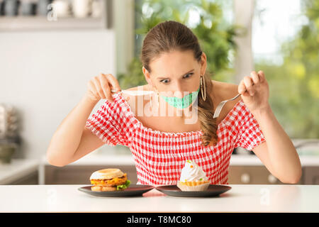 Emotionale Frau mit Maßband um den Mund und ungesundes Essen in der Küche. Diät Konzept Stockfoto