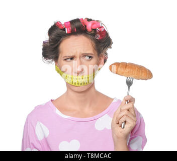 Emotionale Frau mit Maßband um den Mund und leckeres Croissant auf weißem Hintergrund. Diät Konzept Stockfoto