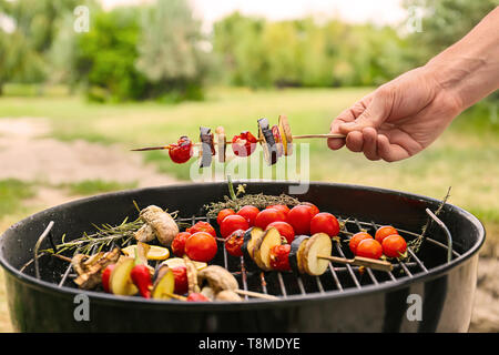 Mann hält Spieß mit Gemüse über Grill im Freien Stockfoto