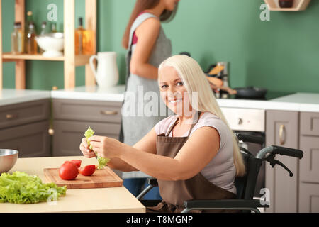 Reife Frau im Rollstuhl zusammen kochen mit Tochter zu Hause Stockfoto