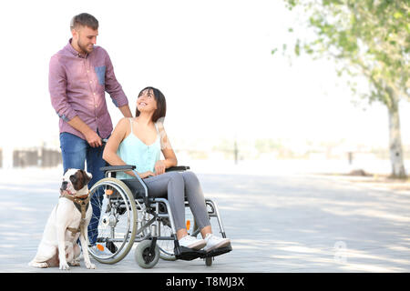 Junge Frau im Rollstuhl mit ihrem Mann und der Hund im Freien Stockfoto