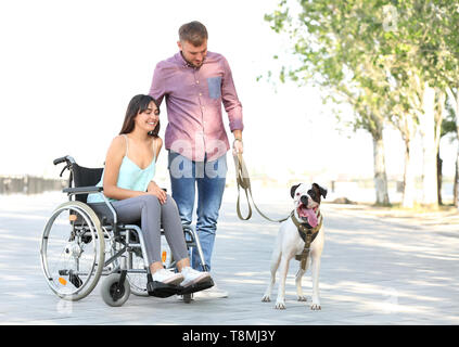 Junge Frau im Rollstuhl mit ihrem Mann und der Hund im Freien Stockfoto