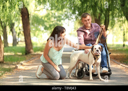 Junger Mann im Rollstuhl mit seiner Frau und Hund im Freien Stockfoto