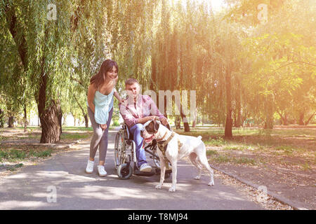 Junger Mann im Rollstuhl mit seiner Frau und Hund im Freien Stockfoto