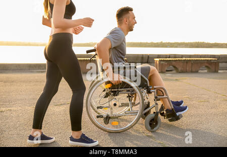 Junger Mann im Rollstuhl und sportliche Frau Training im Freien Stockfoto