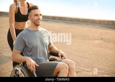 Sportliche Frau helfen jungen Mann im Rollstuhl im Freien Stockfoto