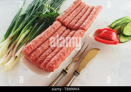 Chevapchichi ist eine nationale Balkan Teller. Nahaufnahme einer Reihe von frischem rohem Rindfleisch Döner auf einem weißen rechteckigen Platte. Stockfoto