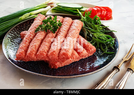 Chevapchichi ist eine nationale Balkan Teller. Nahaufnahme einer Reihe von frischem rohem Rindfleisch Döner auf schwarzem Teller. Stockfoto