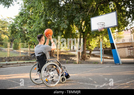 Junger Mann im Rollstuhl Basketball spielen im Freien Stockfoto