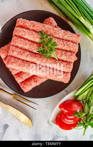 Chevapchichi ist eine nationale Balkan Teller. Nahaufnahme einer Reihe von frischem rohem Rindfleisch Döner auf schwarzem Teller. Stockfoto