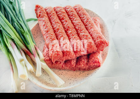 Chevapchichi ist eine nationale Balkan Teller. Nahaufnahme einer Reihe von frischem rohem Rindfleisch Döner auf einem weißen rechteckigen Platte. Stockfoto