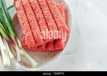 Chevapchichi ist eine nationale Balkan Teller. Nahaufnahme einer Reihe von frischem rohem Rindfleisch Döner auf einem weißen rechteckigen Platte. Stockfoto