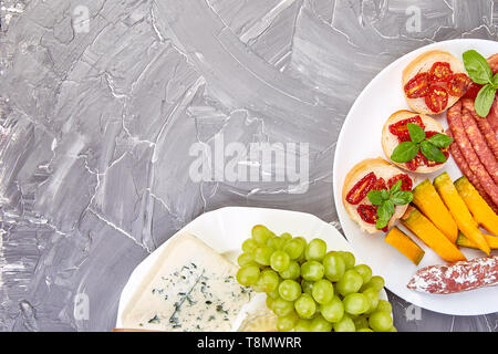Italienische Antipasti Wein Snacks. Antipasti mit ruckartiger, Salami, Käse, Trauben, Oliven, Essiggurken Melone, Brushettas auf grunge grauen Hintergrund. Italienisch Stockfoto
