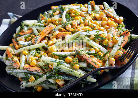 Gurke mais Käse Salat mit Joghurt Zitrone Dressing mit fein gehackten Dill auf einer schwarzen Platte auf einer konkreten Tabelle, Ansicht von oben, Schließen - Stockfoto