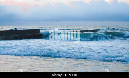 Meer, Strand, Pier, Odessa, Ukraine. Blaues Wasser mit gewellten Textur und weiße Spritzer in der Nähe von Old betonsteine am Strand des Schwarzen Meeres Stockfoto