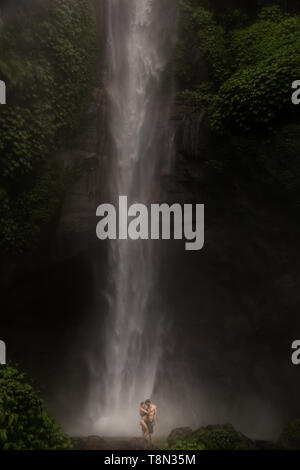 Junge Paar genießt die Frische der Natur unter einem Wasserfall in den Tropen. Das junge Paar umarmen und küssen unter dem Wasserfall. Stockfoto