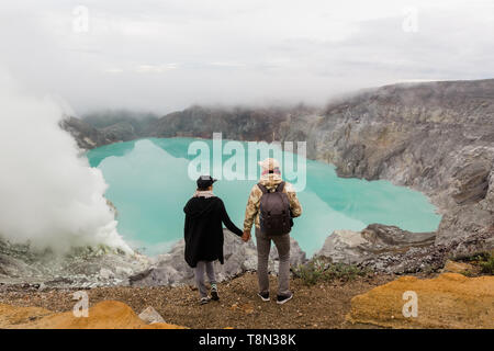 Paar Touristen betrachtet die Schwefel See auf dem Ijen Vulkan auf der Insel Java in Indonesien. Wanderer auf Top Mountain - Konzept Stockfoto