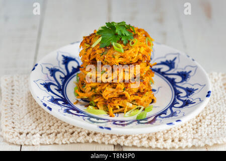 Ein Stapel mit vier süße Kartoffeln und Karotten rostis auf einem blauen und weißen Teller. Stockfoto