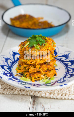 Ein Stapel mit vier süße Kartoffeln und Karotten rostis auf einem blauen und weißen Teller. Stockfoto